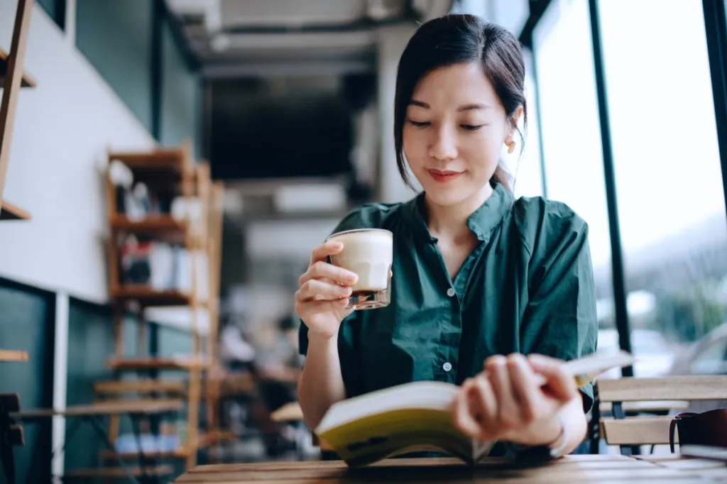 Young Asian woman taking a break, having a quiet time enjoying a cup of coffee and reading book in cafe